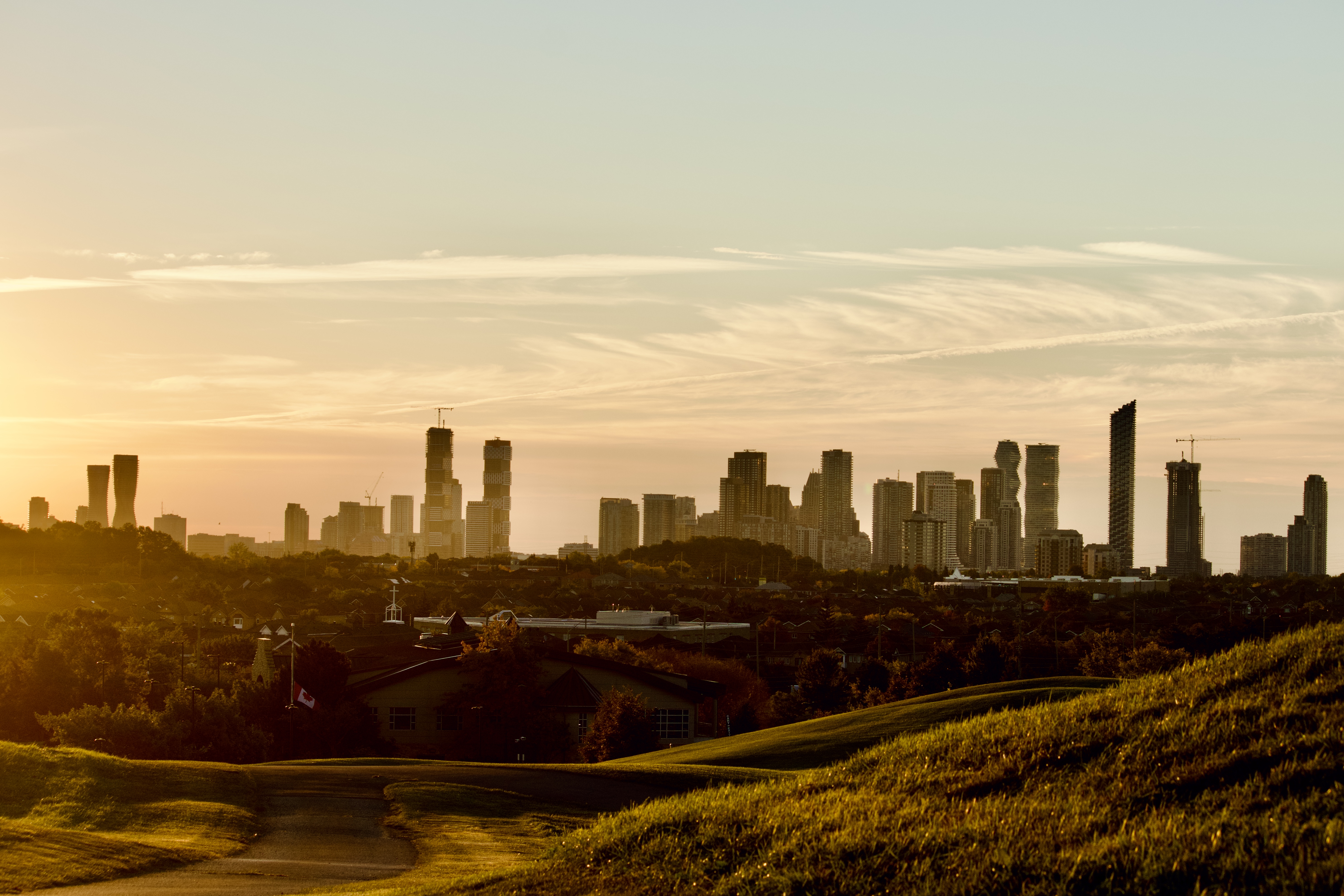 Golden hour dawn illumination across rolling green hills towards the silhouette of Mississauga City Centre skyline